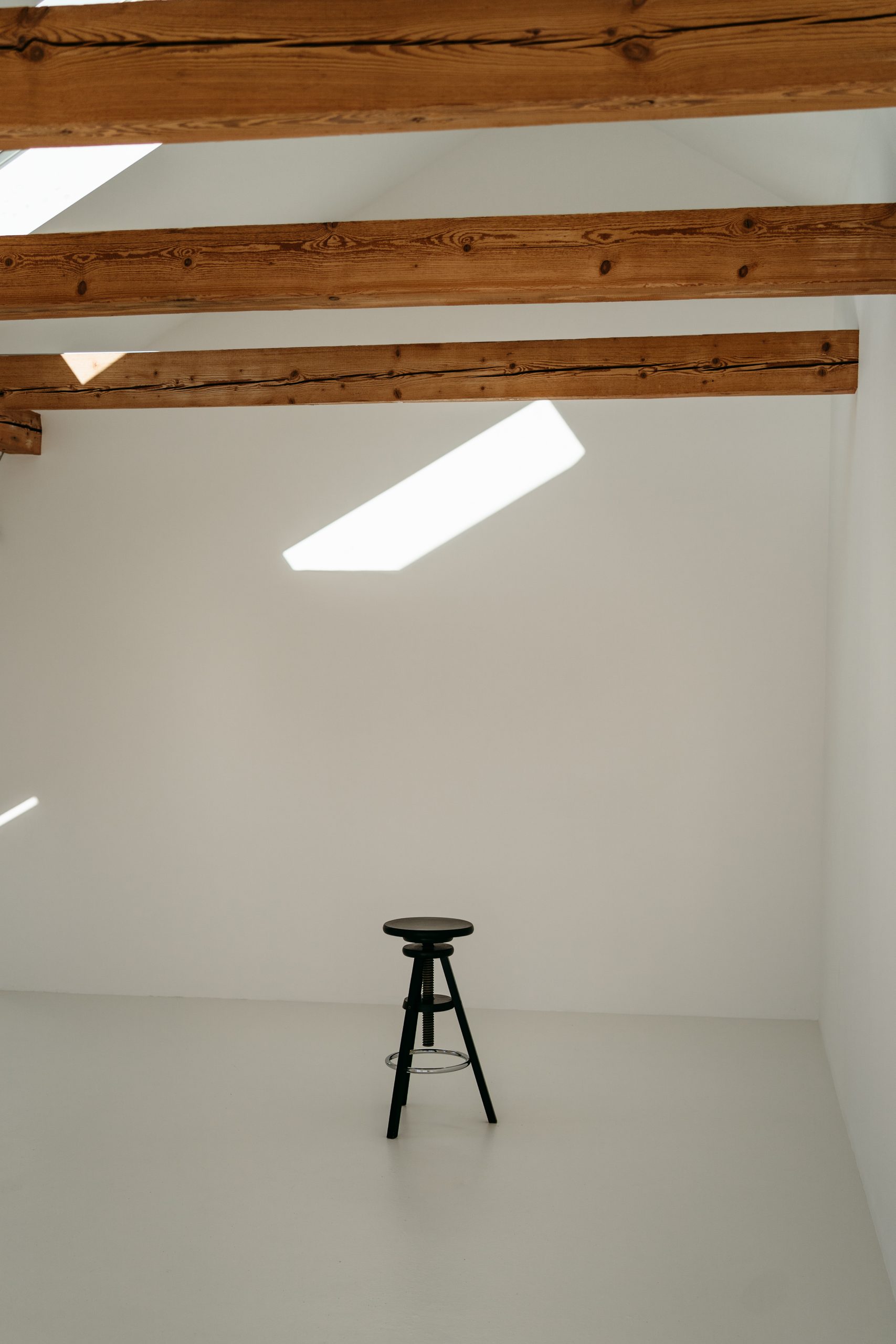 Foto aus dem studio liz. Im Fokus ist ein schwarzer Hocker. Oben sind die Holzbalken zu sehen.