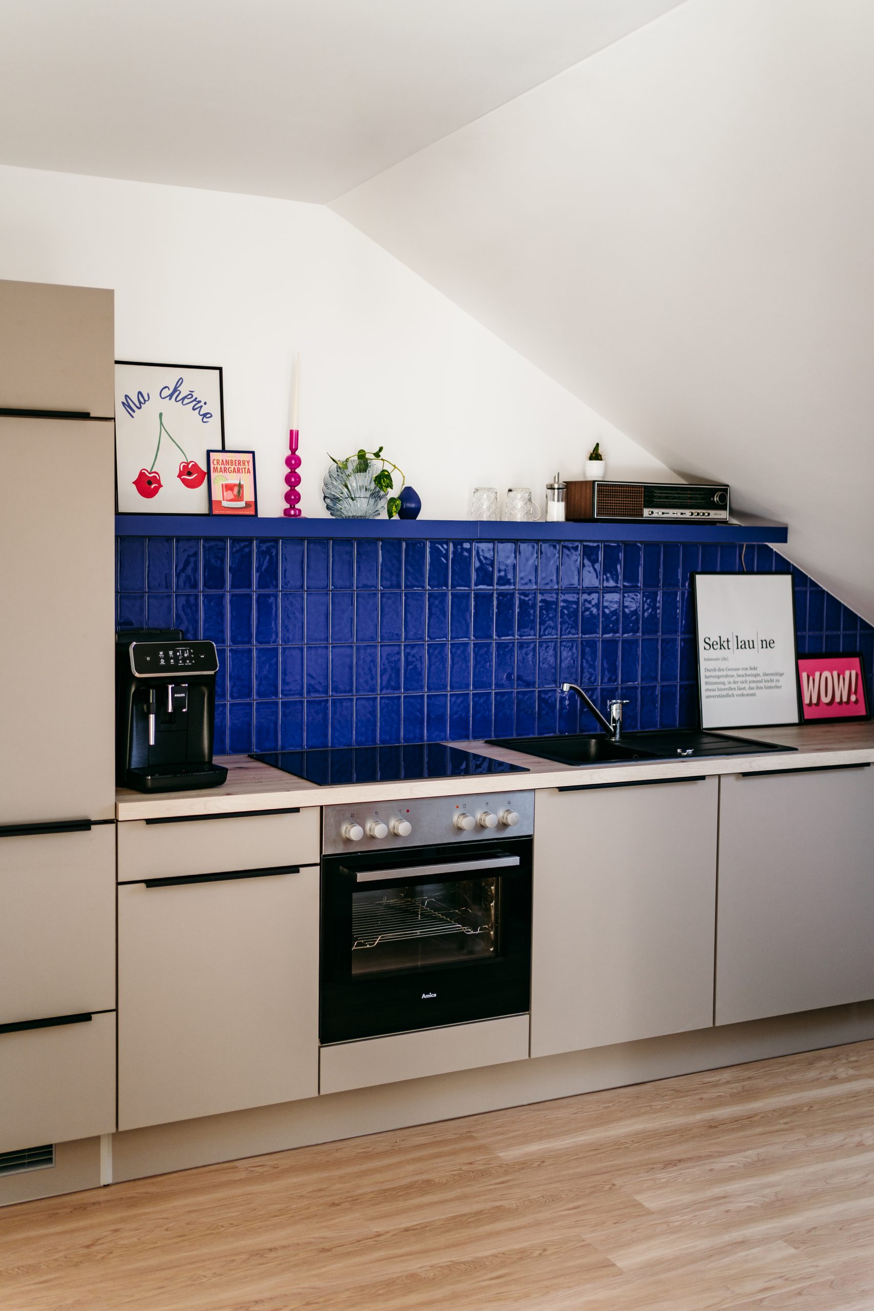 Foto von der Küche im studio liz. Die Küchenzeile hat beige Fronten und an der Wand sind dunkelblaue Fließen.