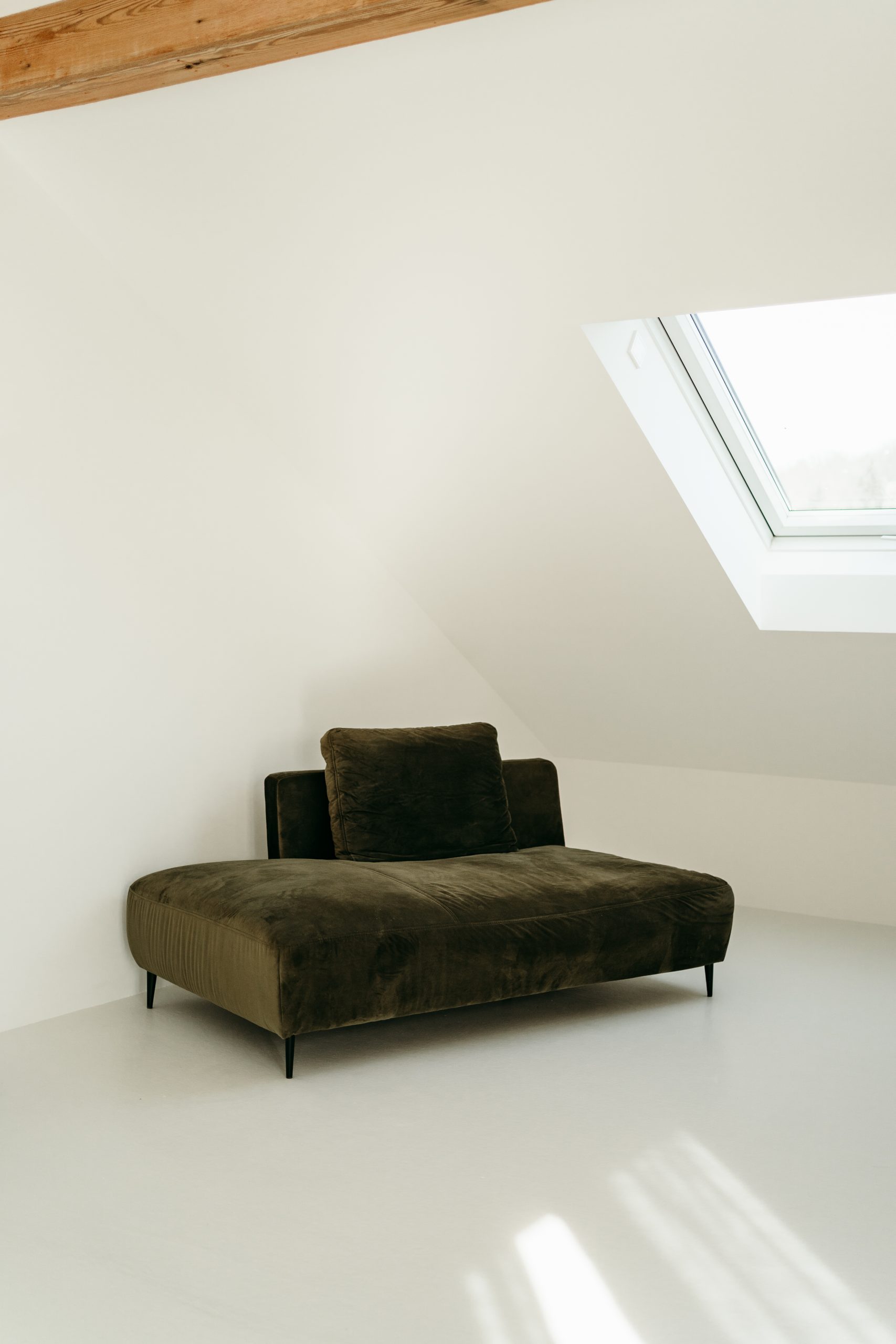 Foto aus dem studio liz. Unter einem Dachfenster steht ein dunkelgrünes Sofa.